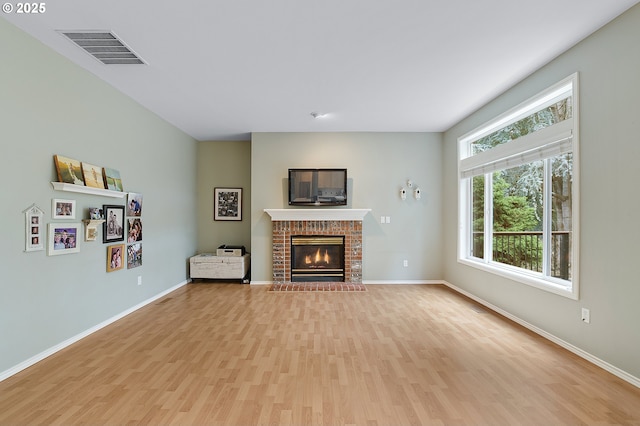 unfurnished living room featuring baseboards, light wood finished floors, a brick fireplace, and visible vents