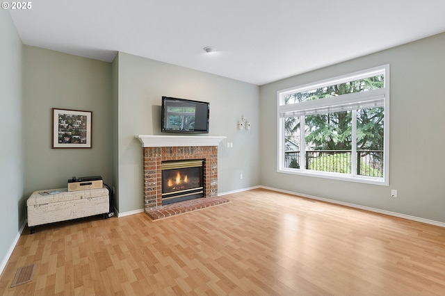 unfurnished living room featuring visible vents, baseboards, light wood finished floors, and a brick fireplace