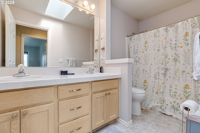 full bath featuring a sink, toilet, double vanity, a skylight, and tile patterned flooring