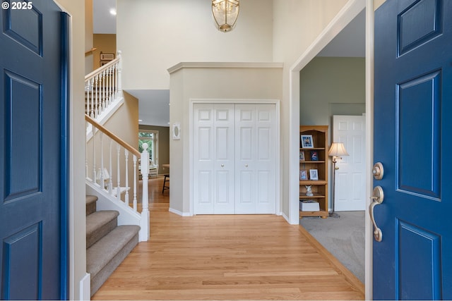 entrance foyer featuring light wood-type flooring, a towering ceiling, baseboards, and stairs