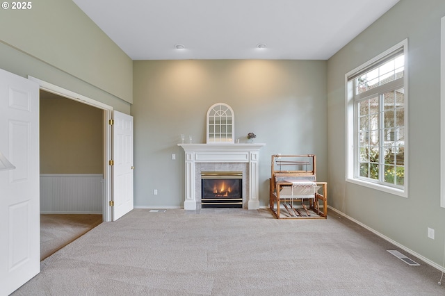 unfurnished living room with a premium fireplace, visible vents, carpet, and a wealth of natural light