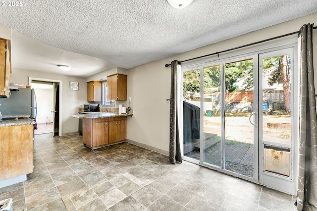 9304 NE 96th St, Vancouver, WA 98662 - kitchen featuring brown cabinets, a peninsula, a textured ceiling, freestanding refrigerator, and stainless steel microwave