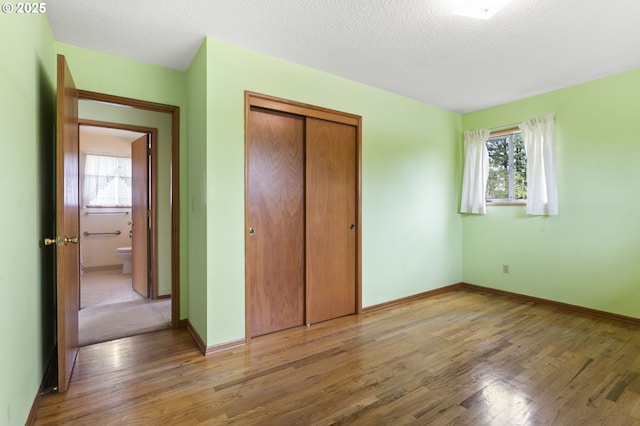 unfurnished bedroom with wood finished floors, a closet, baseboards, and a textured ceiling