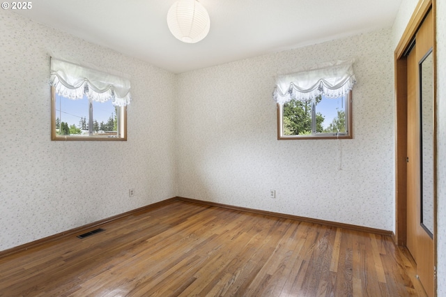 unfurnished bedroom with hardwood / wood-style floors, wallpapered walls, a closet, and baseboards