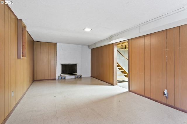 finished basement with tile patterned floors, a fireplace, stairs, a textured ceiling, and wooden walls