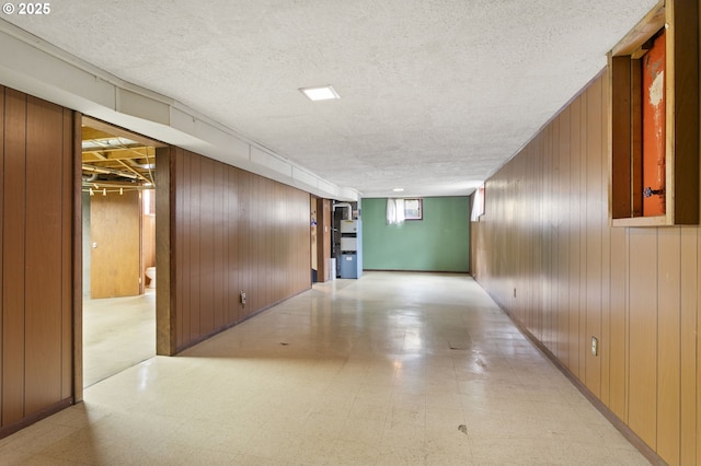 corridor with light flooring, wood walls, and a textured ceiling