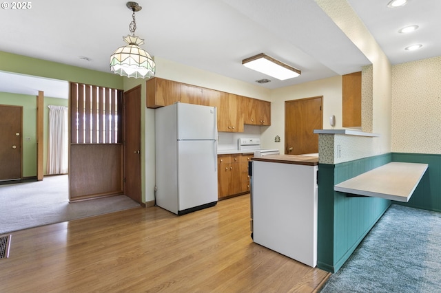 kitchen with white appliances, a peninsula, brown cabinetry, light wood finished floors, and decorative light fixtures