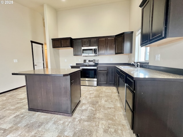 kitchen featuring baseboards, a kitchen island, a high ceiling, a sink, and appliances with stainless steel finishes