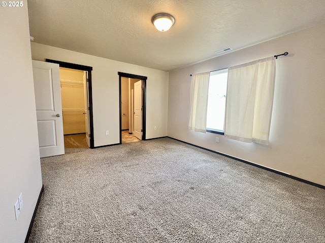 unfurnished bedroom featuring baseboards, visible vents, a spacious closet, a textured ceiling, and carpet flooring