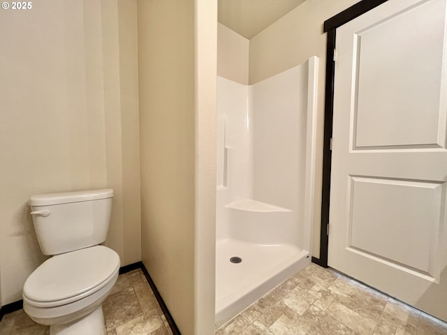 full bath with baseboards, toilet, a shower stall, and stone finish floor