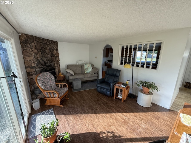 living room featuring a textured ceiling, a stone fireplace, and hardwood / wood-style floors