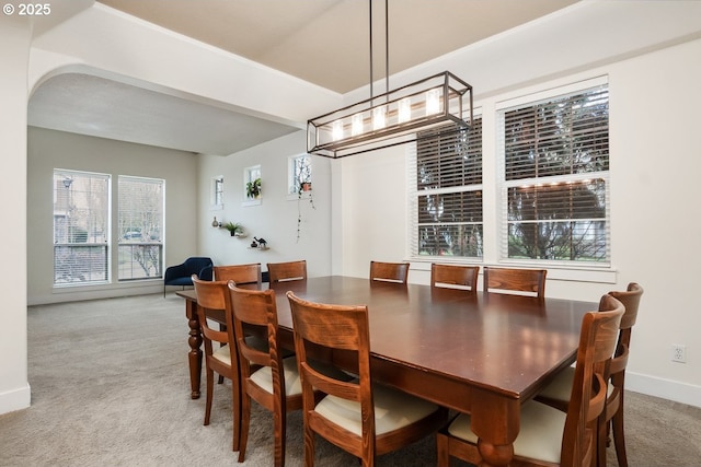 dining room featuring baseboards, light carpet, and arched walkways