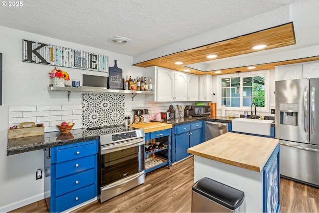 kitchen featuring stainless steel appliances, butcher block counters, blue cabinets, open shelves, and a textured ceiling