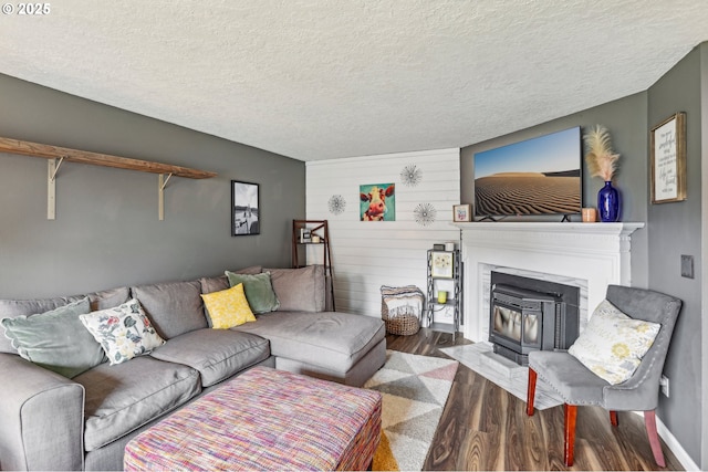 living room featuring wood finished floors, a textured ceiling, a wood stove, wooden walls, and baseboards