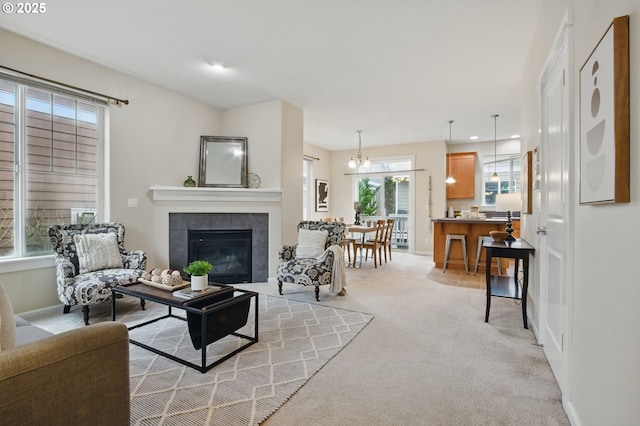 living area with baseboards, light carpet, an inviting chandelier, and a tiled fireplace