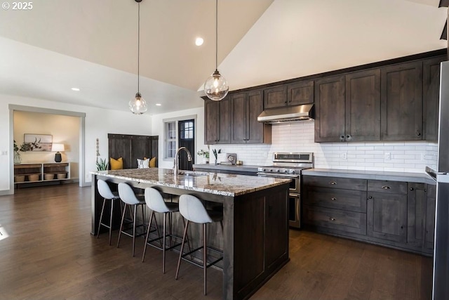 kitchen with a breakfast bar, decorative light fixtures, stainless steel range, an island with sink, and light stone countertops