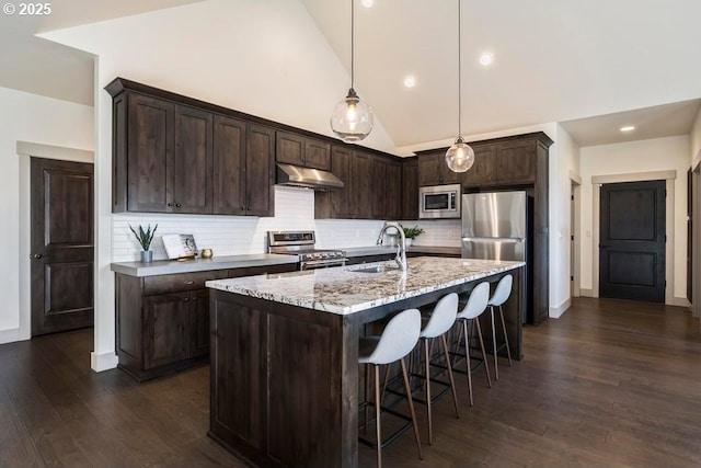 kitchen featuring sink, appliances with stainless steel finishes, a kitchen island with sink, light stone counters, and decorative light fixtures