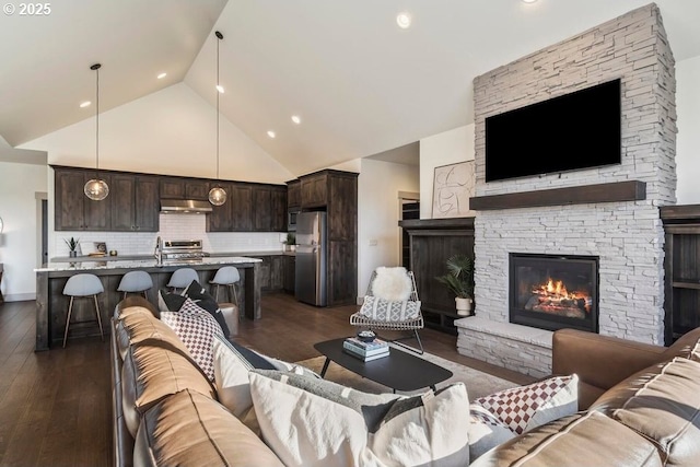 living room with high vaulted ceiling, dark wood-type flooring, sink, and a fireplace