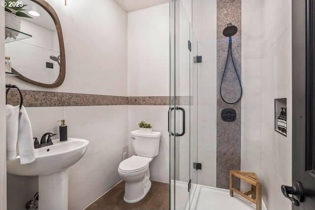 bathroom featuring toilet, a shower with shower door, and tile walls