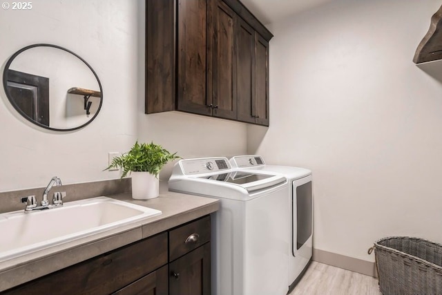 washroom featuring cabinets, washing machine and dryer, sink, and light hardwood / wood-style floors