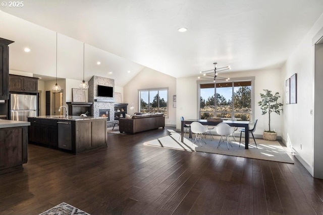 dining area with vaulted ceiling, a stone fireplace, sink, dark hardwood / wood-style flooring, and a notable chandelier