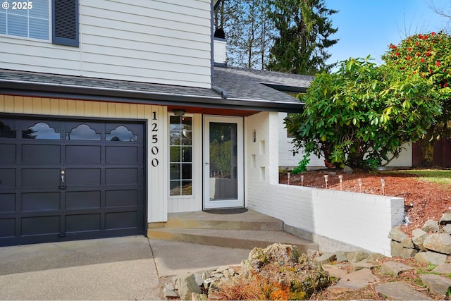 entrance to property featuring concrete driveway, a garage, and roof with shingles