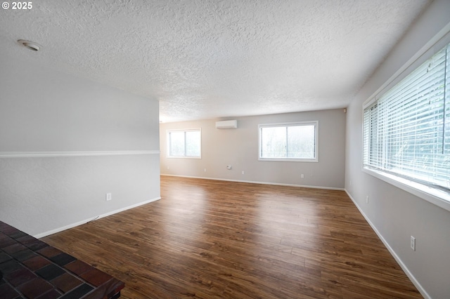 unfurnished room featuring a healthy amount of sunlight, baseboards, a wall unit AC, and dark wood-style flooring