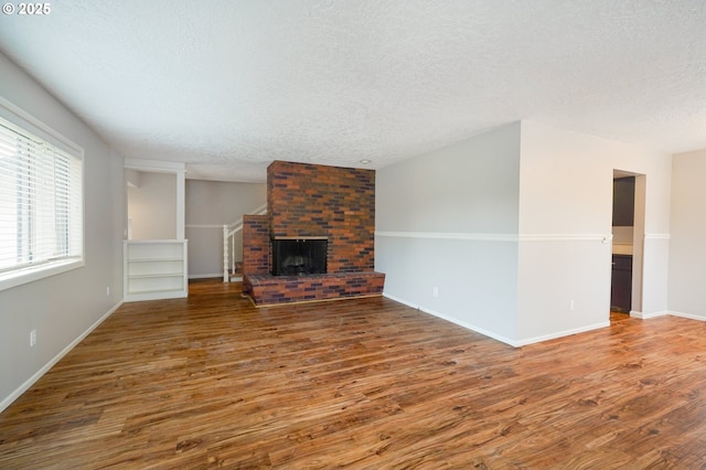 unfurnished living room featuring a fireplace, a textured ceiling, baseboards, and wood finished floors