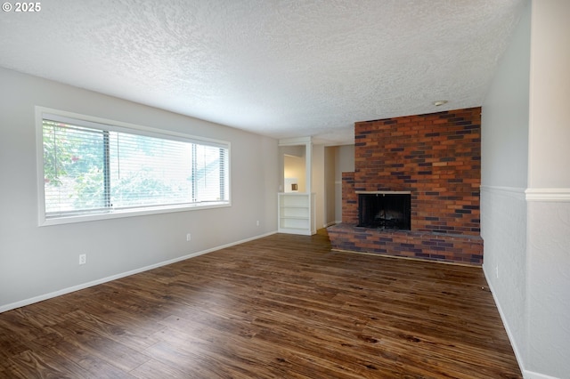 unfurnished living room featuring dark wood finished floors, a brick fireplace, and a textured ceiling