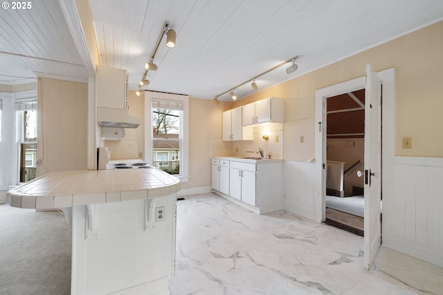 kitchen with tile counters, electric range oven, marble finish floor, under cabinet range hood, and white cabinetry