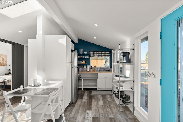 kitchen with lofted ceiling, stainless steel fridge, white cabinets, hardwood / wood-style flooring, and gas cooktop