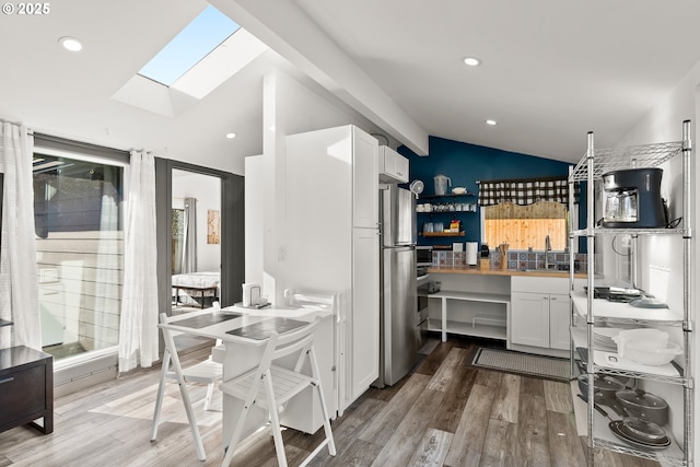 kitchen with white cabinetry, lofted ceiling with skylight, hardwood / wood-style floors, and stainless steel refrigerator