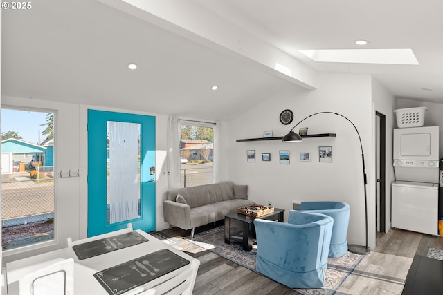 living room with stacked washer / drying machine, vaulted ceiling with skylight, and light wood-type flooring