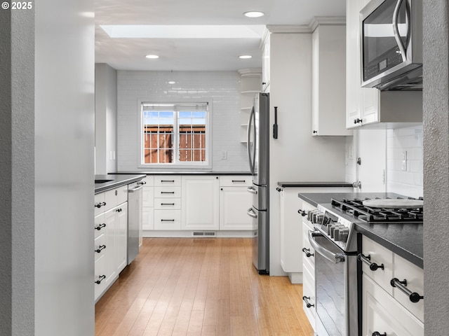 13145 SW 61st Ave, Portland, OR 97219 - kitchen featuring stainless steel appliances, dark countertops, tasteful backsplash, white cabinets, and light wood-style floors
