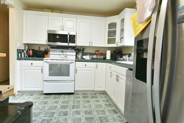 5902 NE 11th Ave, Portland, OR 97211 - kitchen featuring stainless steel appliances, tile countertops, white cabinetry, and glass insert cabinets