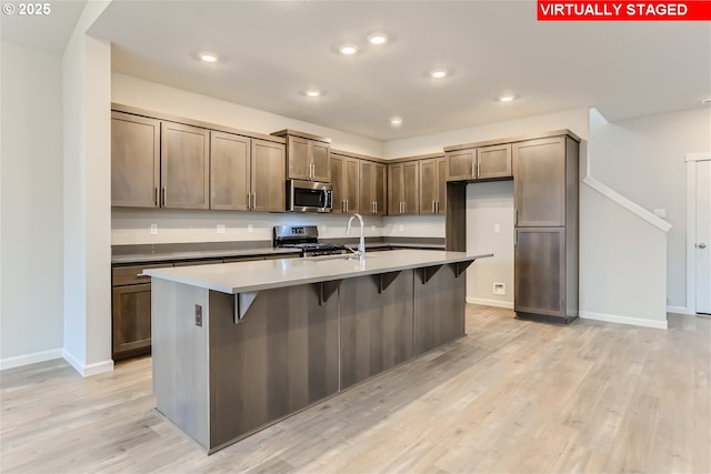 kitchen with light wood finished floors, baseboards, a kitchen island with sink, stainless steel appliances, and recessed lighting