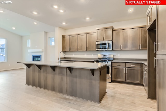 kitchen with a center island with sink, appliances with stainless steel finishes, light wood-style floors, a sink, and recessed lighting