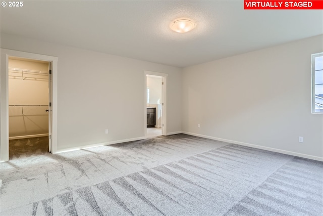 unfurnished bedroom featuring light carpet, a walk in closet, a closet, and ensuite bathroom