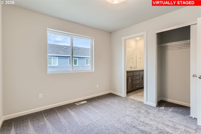 unfurnished bedroom with light colored carpet, connected bathroom, a closet, and sink