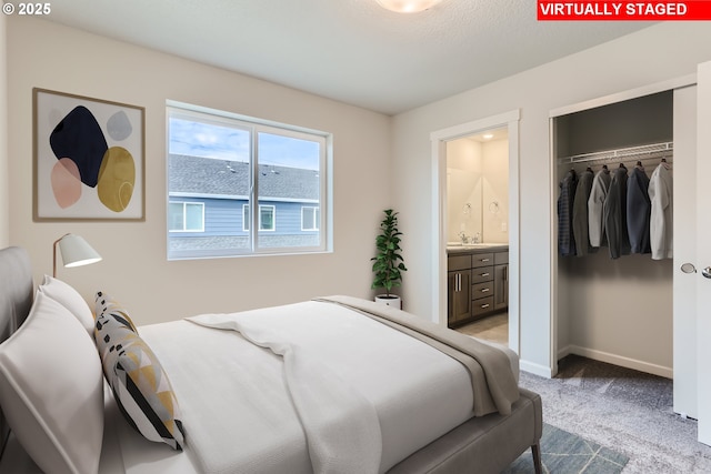 bedroom featuring carpet, a closet, ensuite bathroom, a sink, and baseboards