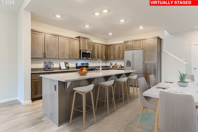 kitchen with stainless steel appliances, a kitchen bar, light hardwood / wood-style flooring, and a kitchen island with sink