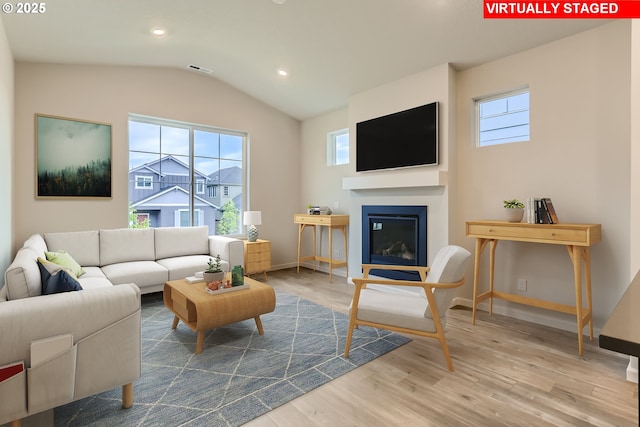 living area with lofted ceiling, baseboards, wood finished floors, and a glass covered fireplace