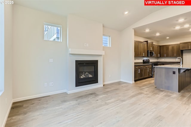 kitchen with a kitchen breakfast bar, stainless steel appliances, light hardwood / wood-style floors, and a kitchen island with sink