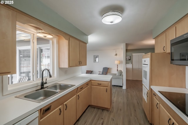 kitchen with light brown cabinets, a peninsula, white appliances, and a sink