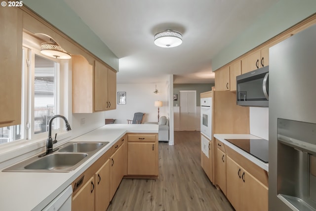 kitchen with appliances with stainless steel finishes, a peninsula, light countertops, light brown cabinetry, and a sink