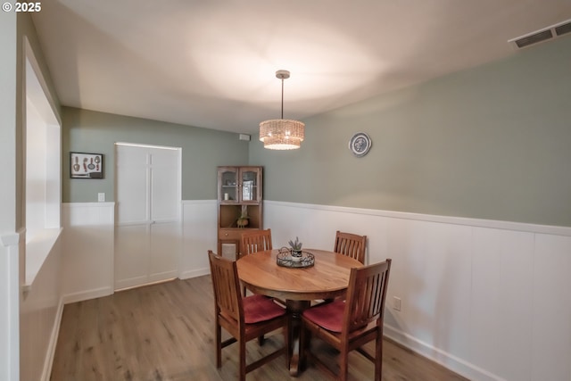 dining space with visible vents, wood finished floors, and wainscoting