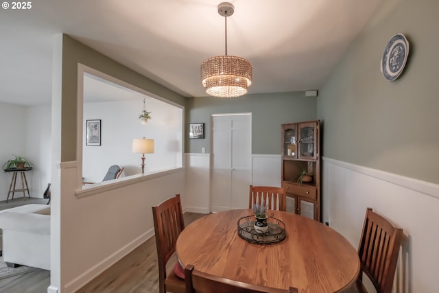 dining area with wainscoting, wood finished floors, and an inviting chandelier