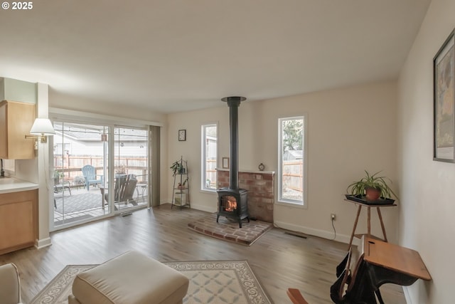 living area with a wood stove, visible vents, light wood-style flooring, and baseboards