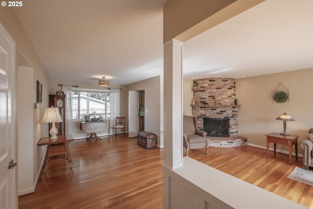 living area featuring ornate columns, a fireplace, baseboards, and wood finished floors