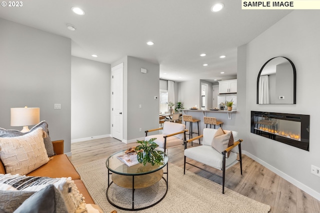 living room with recessed lighting, baseboards, light wood finished floors, and a glass covered fireplace